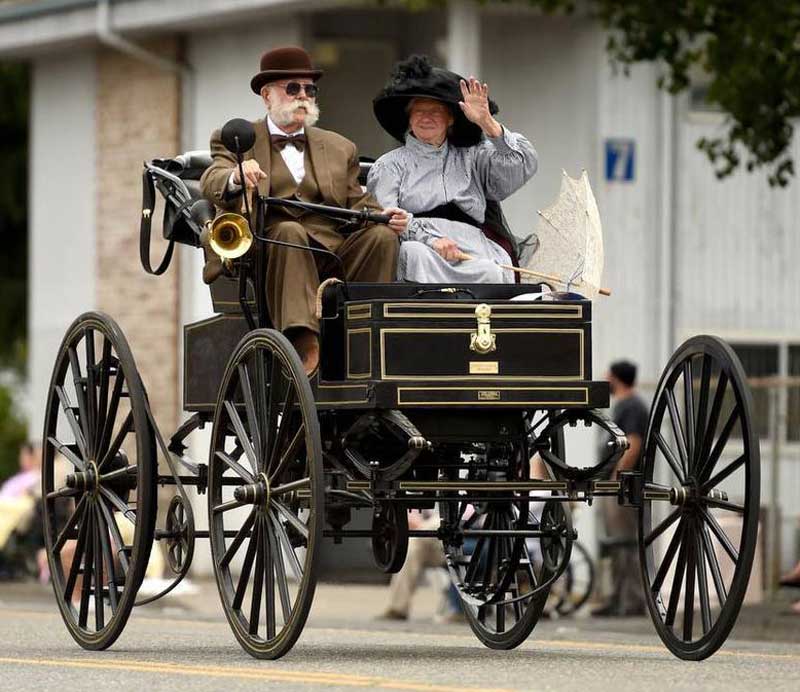 Man and woman wearing period costumes while driving brass era automobile